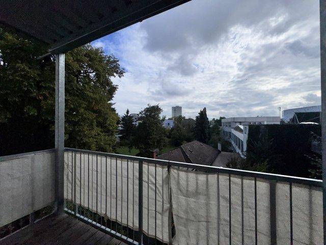Balkon mit Metallgeländer und weitem Blick über grüne Bäume und die Umgebung.