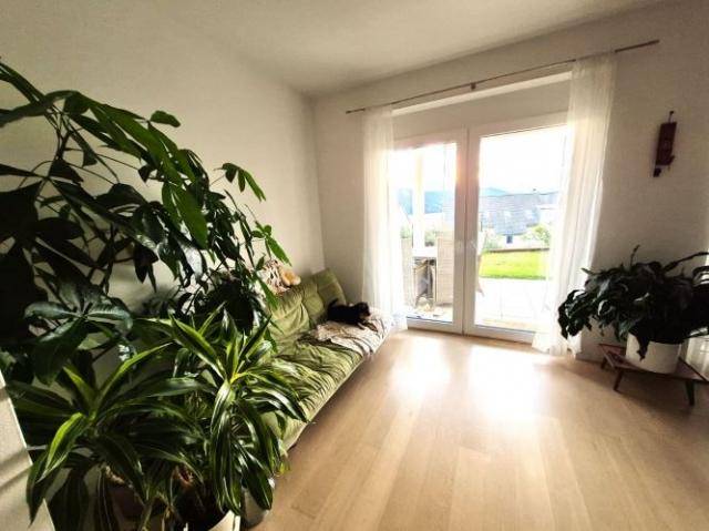 Helles Wohnzimmer mit vielen Grünpflanzen, Holzboden und Zugang zu einem kleinen Gartenbereich.