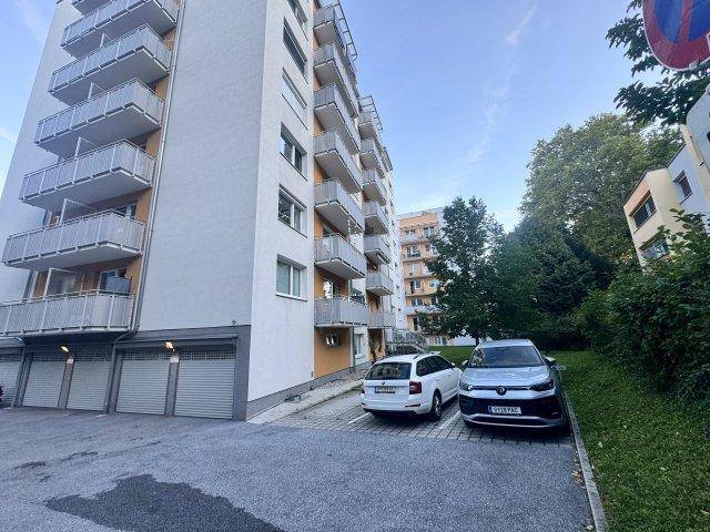 Mehrstöckiges Wohngebäude mit zahlreichen Balkonen und Parkplätzen im Freien.