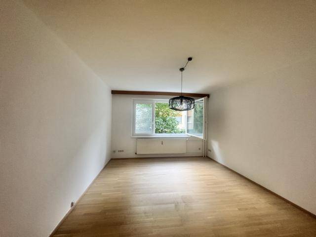Geräumiges Zimmer mit Parkettboden und großem Fenster mit Blick ins Grüne.