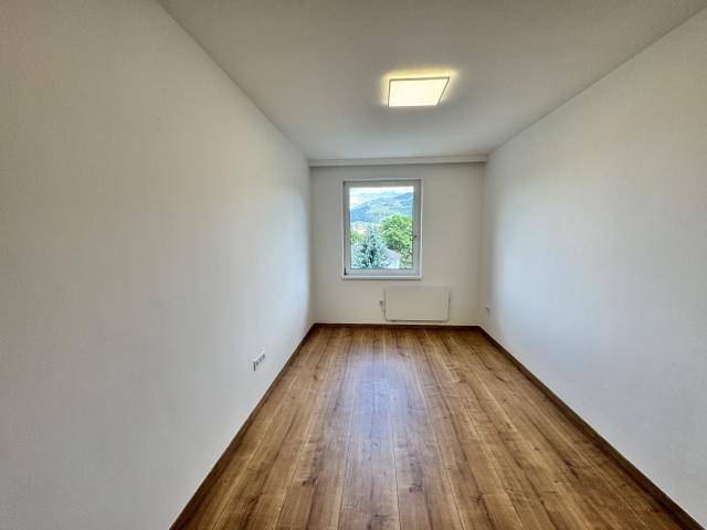 Langes, helles Zimmer mit Laminatboden und einem Fenster am Ende, das einen grünen Ausblick bietet.