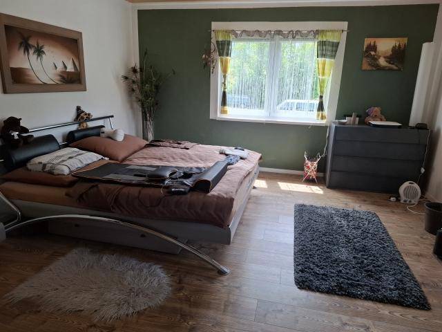 Gemütliches Schlafzimmer mit Laminatboden, grünen Wänden und großem Fenster mit Blick ins Grüne.