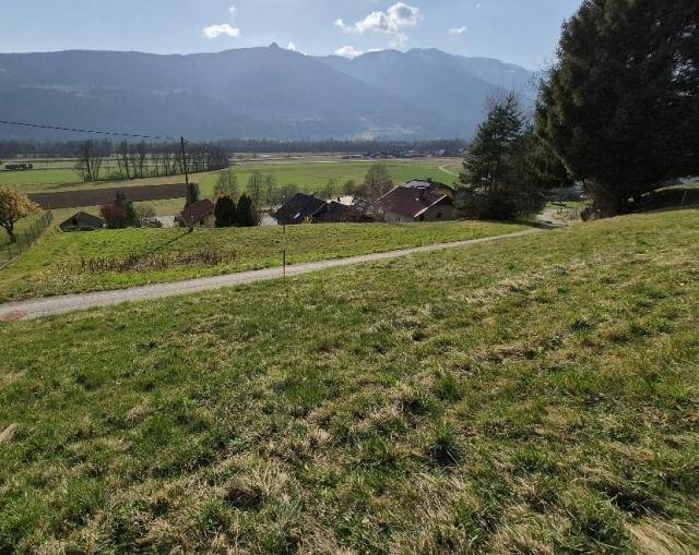Weitläufiger Blick von einem grünen Hügel über ein Tal mit Häusern und Bergen in der Ferne.
