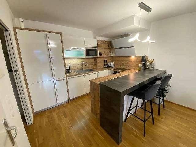 Moderne Küche mit weißen Hochglanzfronten, Holzakzenten und einer integrierten Frühstücksbar.