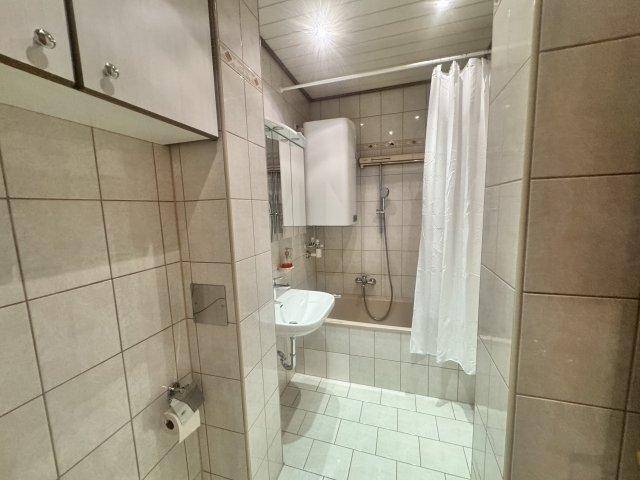 Kleines Badezimmer mit Badewanne, Duschvorhang, Waschbecken und hellen Fliesen.