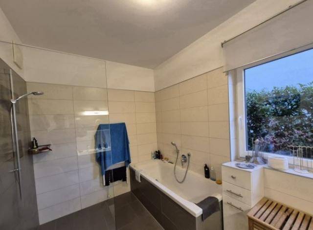 Modernes Badezimmer mit Badewanne, begehbarer Dusche und Fenster für natürliches Tageslicht.