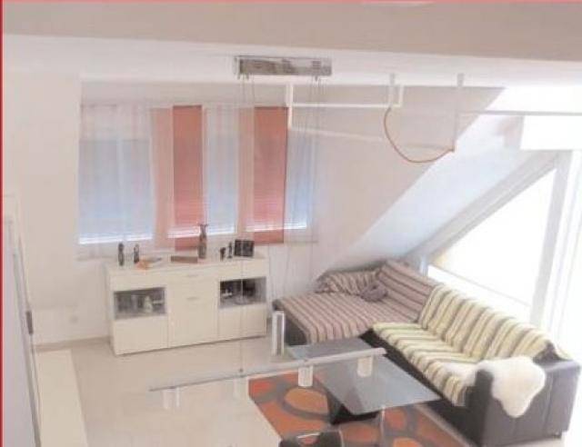 Gemütliches Wohnzimmer im Dachgeschoss mit Schrägen, Sofa und Fenster.