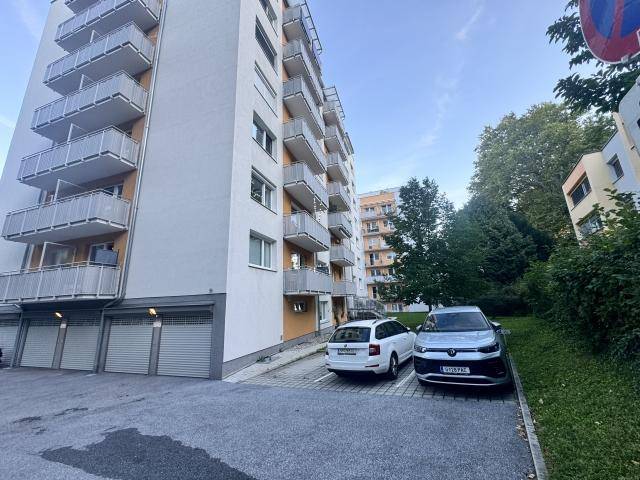 Mehrstöckiges Wohngebäude mit zahlreichen Balkonen und Parkplätzen im Freien.
