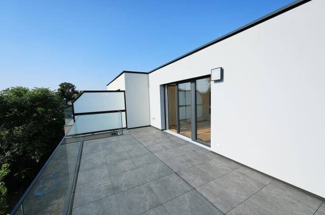 Geräumige Dachterrasse mit modernen grauen Fliesen und Glasgeländer, ideal zum Entspannen im Freien.