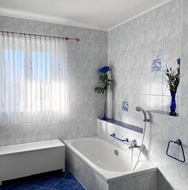 Helles Badezimmer mit hellblauen Fliesen, Badewanne und Fenster für Tageslicht.