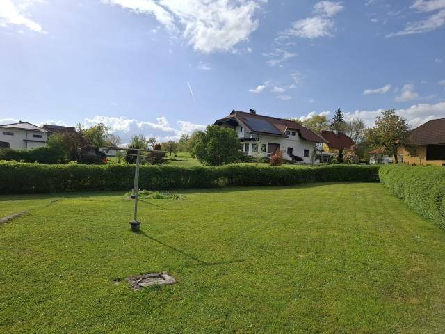 Gepflegter Garten mit großer Rasenfläche und Hecke unter blauem Himmel mit Wolken.
