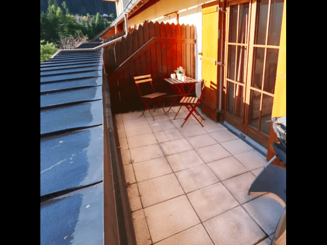 Balkon mit Fliesenboden, Holzwänden und einem kleinen Tisch mit Stühlen.