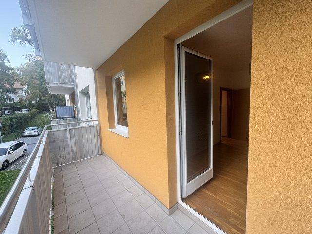 Balkon mit Fliesenboden, Metallgeländer und Blick auf die Straße sowie umliegende Bäume.