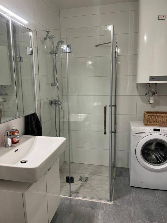 Modernes Badezimmer mit ebenerdiger Dusche, weißen Fliesen und integrierter Waschmaschine.