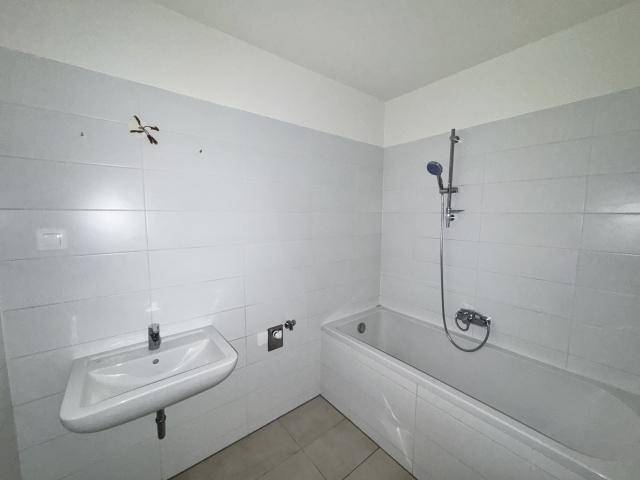 Badezimmer mit weißen Fliesen, Badewanne mit Duschfunktion und Waschbecken.