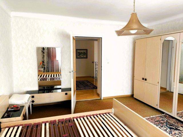 Schlafzimmer mit Teppichboden, Bettgestell und einem Kleiderschrank mit Spiegeltüren.