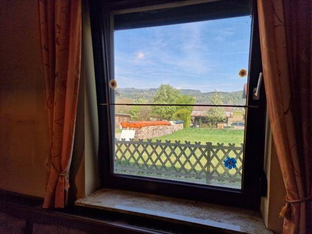 Fensterblick auf die grüne Landschaft und umliegende Häuser unter blauem Himmel.