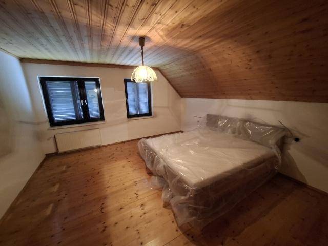 Schlafzimmer im Dachgeschoss mit Holzboden, schräger Decke und neuem Bett mit viel Tageslicht.