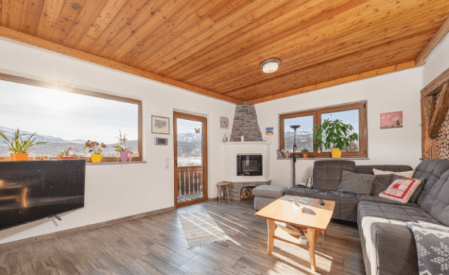 Gemütliches Wohnzimmer mit Holzbalkendecke, Kamin und großen Fenstern mit Panoramablick auf die Berge.