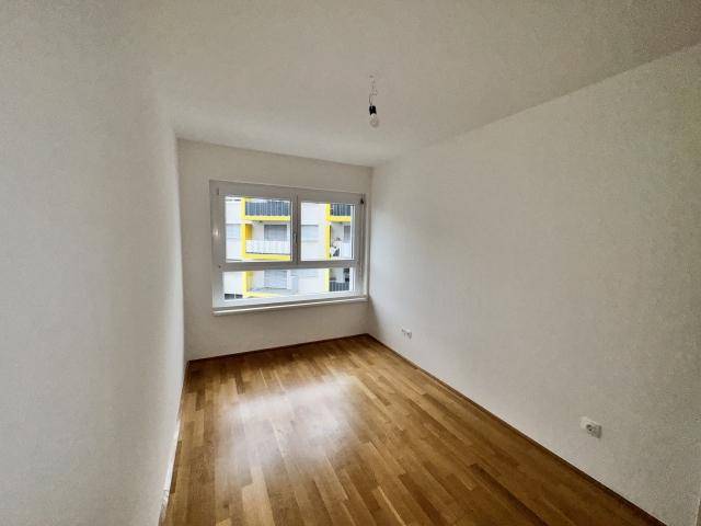 Helles Schlafzimmer mit Parkettboden und Blick auf die umliegenden Gebäude.