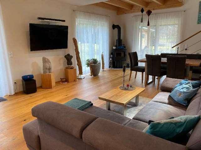 Helles Wohnzimmer mit Holzboden, Kaminofen und sichtbaren Deckenbalken.