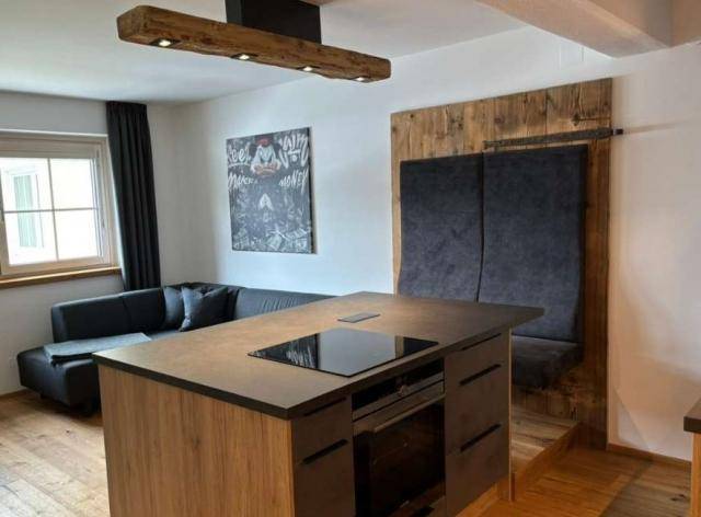 Moderne Kücheninsel mit Induktionskochfeld und Backofen, offen zum Wohnbereich mit Holzelementen.