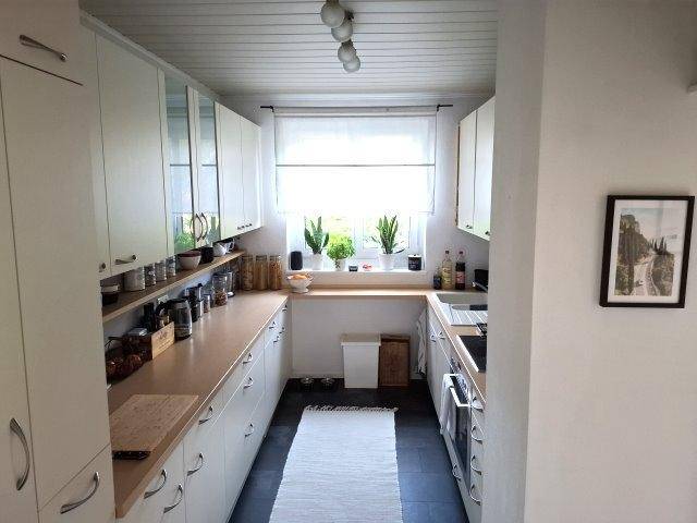 Schmale Küche mit weißen Schränken, Holz-Arbeitsplatten und Fenster.