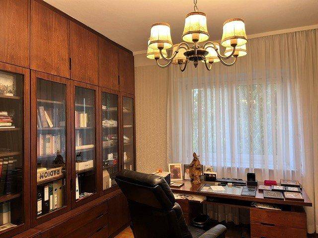 Arbeitszimmer mit großen Holzregalen, Schreibtisch und einem Fenster mit Vorhängen.