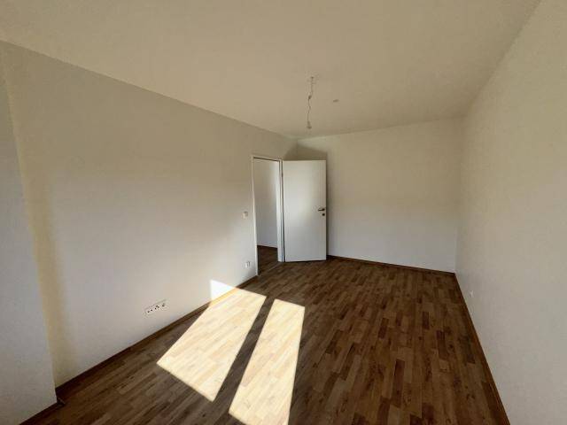 Leeres Schlafzimmer mit hellem Parkettboden und weißen Wänden, das durch die Tür einen weiteren Raum erahnen lässt.