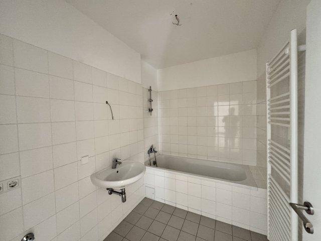 Helles Badezimmer mit weißen Fliesen, Badewanne, Waschbecken und Handtuchheizkörper.