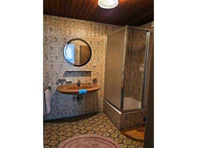 Badezimmer im Stil der 80er Jahre mit gemusterten Fliesen, Waschbecken und Duschkabine.