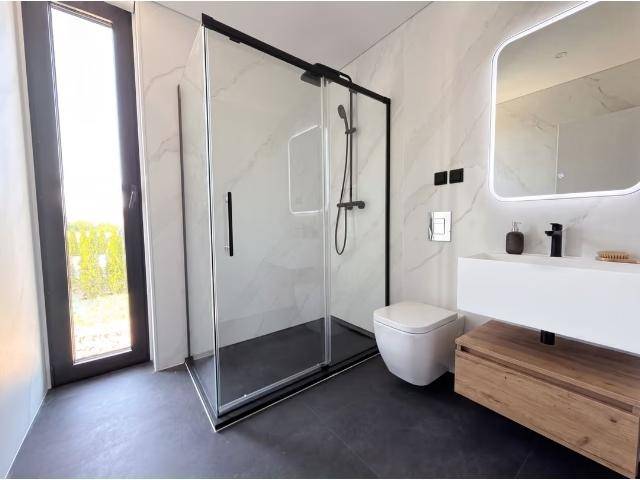 Modernes Badezimmer mit begehbarer Dusche, Wand-WC, Einzelwaschbecken und großem Fenster für natürliches Licht.