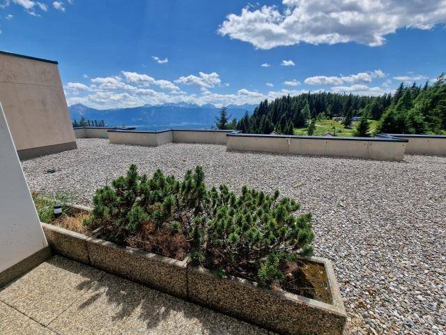 Weitläufige Dachterrasse mit Kiesbelag und atemberaubendem Bergblick unter blauem Himmel.