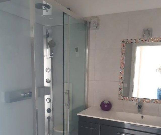 Modernes Badezimmer mit Duschkabine, mehreren Duschdüsen und einem Waschbecken mit Spiegel.