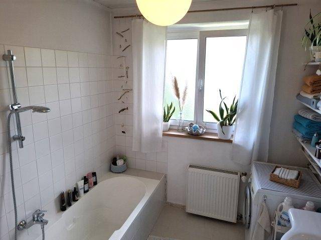 Badezimmer mit Badewanne, weißen Fliesen und Fenster für Tageslicht.
