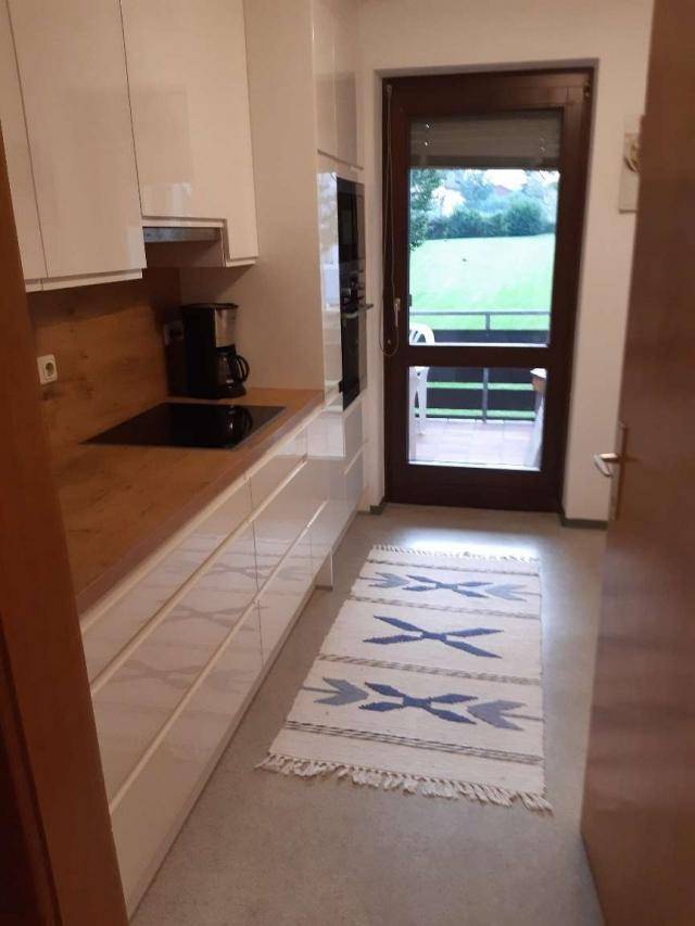Moderne Küche mit weißen Hochglanzfronten, Holzarbeitsplatte und Zugang zum Balkon mit Aussicht.
