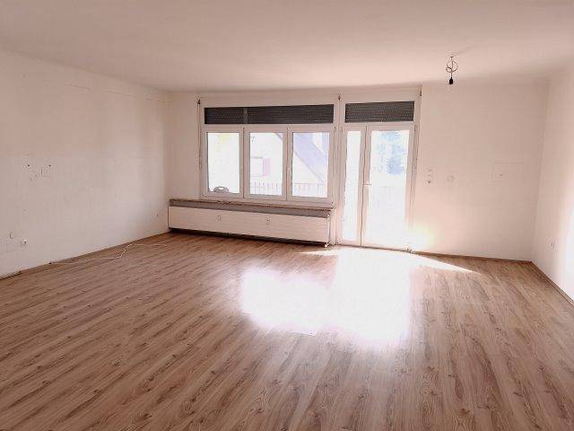 Helles Wohnzimmer mit Laminatboden, großen Fenstern und Zugang zu einem Außenbereich.