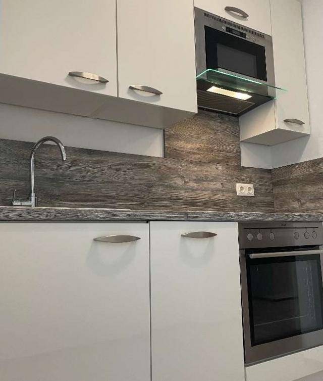 Moderne Einbauküche mit weißen Schränken, integriertem Backofen und Mikrowelle sowie Spülbecken.