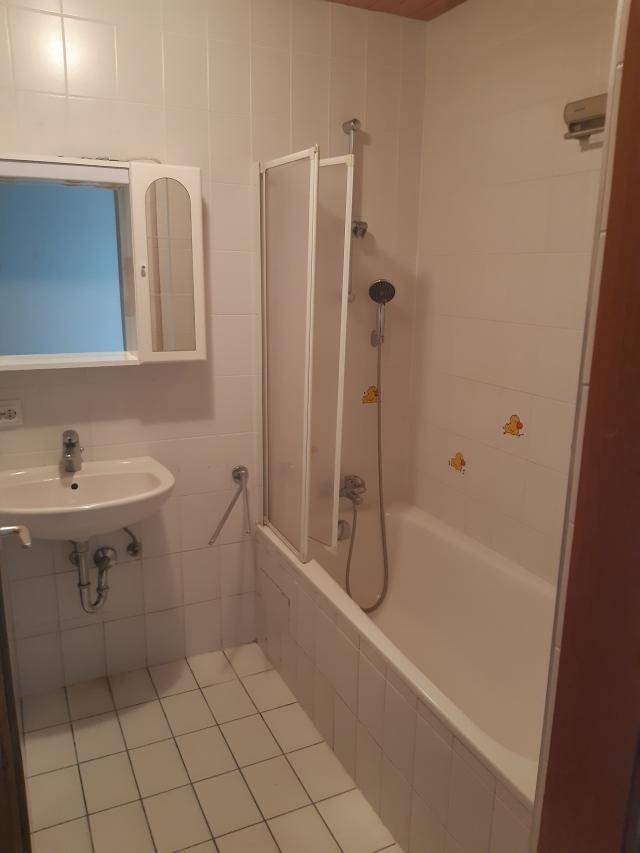 Gefliestes Badezimmer mit Badewanne, Duschabtrennung, Waschbecken und Spiegelschrank.