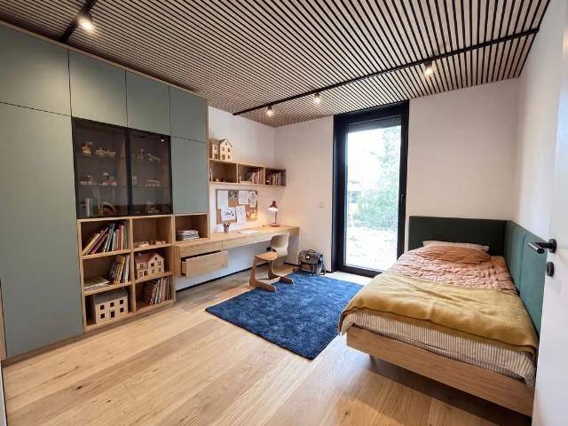 Modernes Schlafzimmer mit Holzboden, integrierten Schränken, Schreibtisch und großem Fenster für viel Tageslicht.