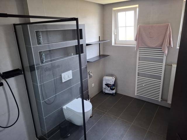 Modernes Badezimmer mit grauen Fliesen, ebenerdiger Dusche und beheiztem Handtuchhalter.