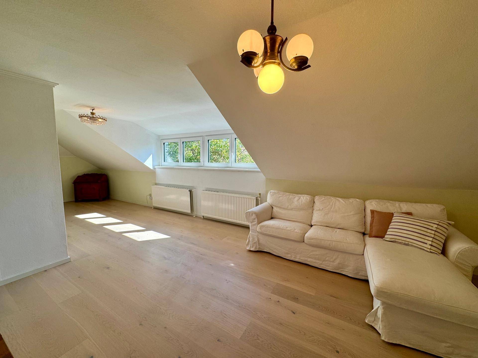Gemütlicher Wohnbereich im Dachgeschoss mit Sofa, Holzboden und charakteristischen Dachschrägen.