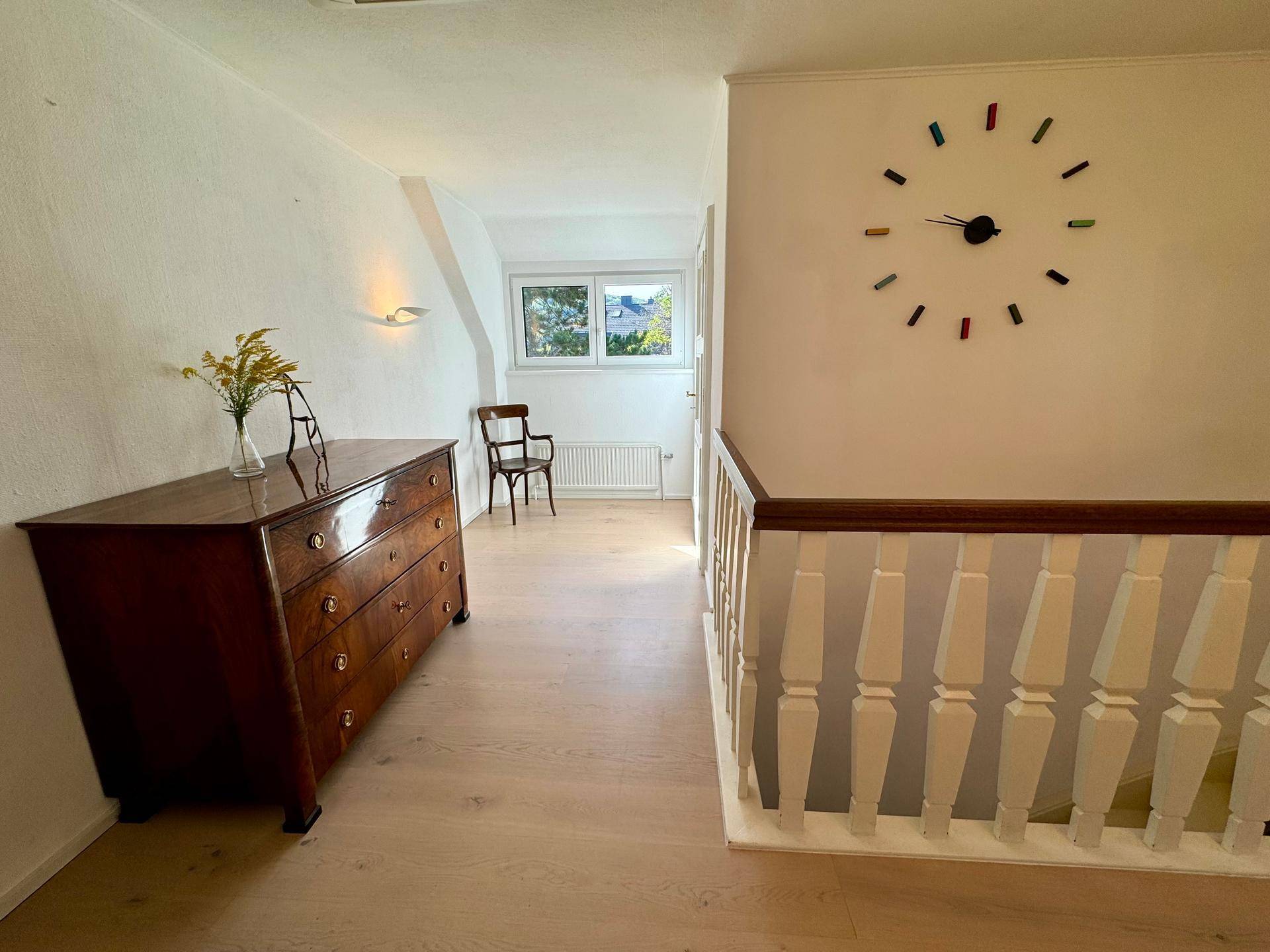 Heller Flur im Obergeschoss mit Holzboden, Kommode und einem Fenster mit Tageslicht.