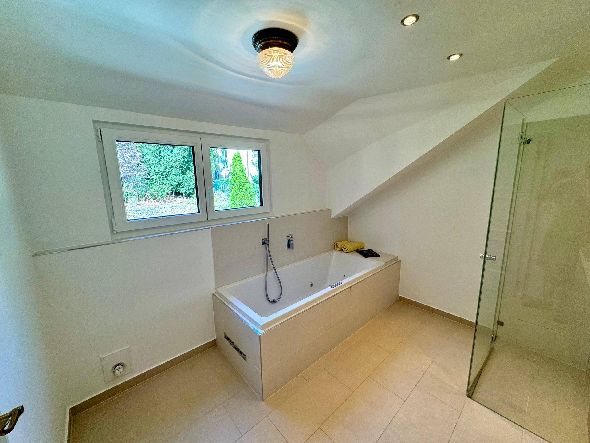 Modernes Badezimmer mit Badewanne, Fenster und hellen Fliesen, ideal zum Entspannen.