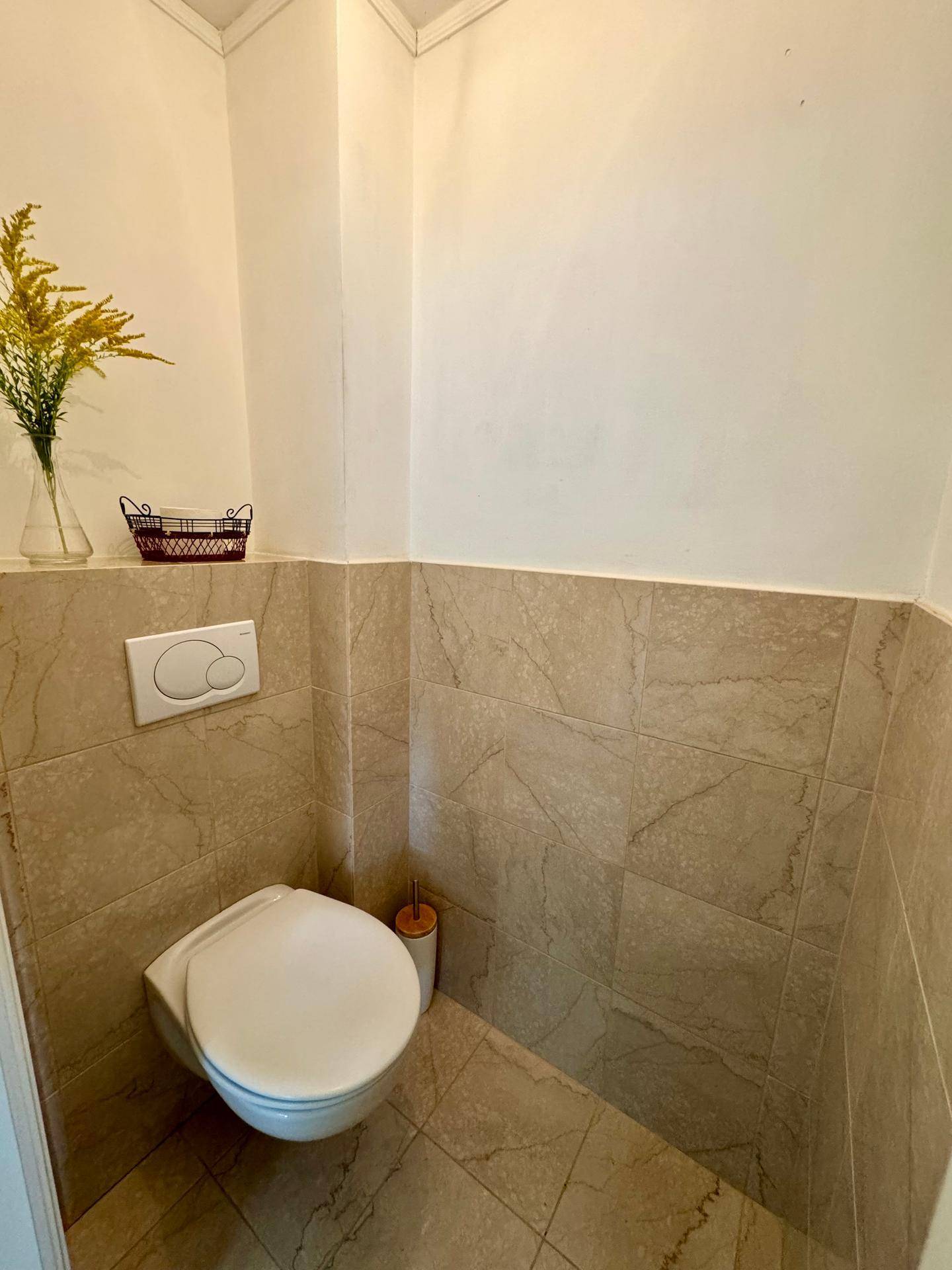 Kleines Gäste-WC mit Wand-WC und beigen Fliesen, schlicht und funktional gestaltet.