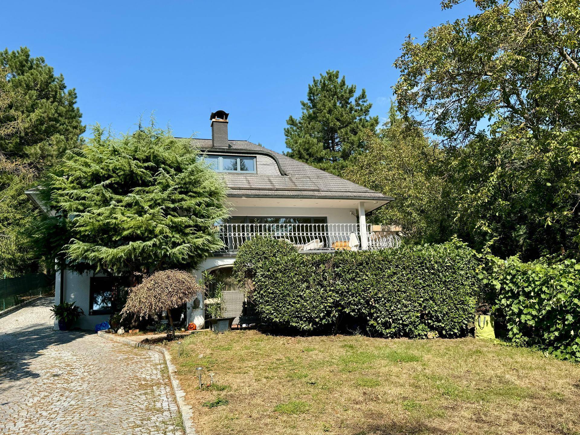 Ansicht des Hauses von außen mit gepflegtem Garten, Balkon und üppiger Vegetation.