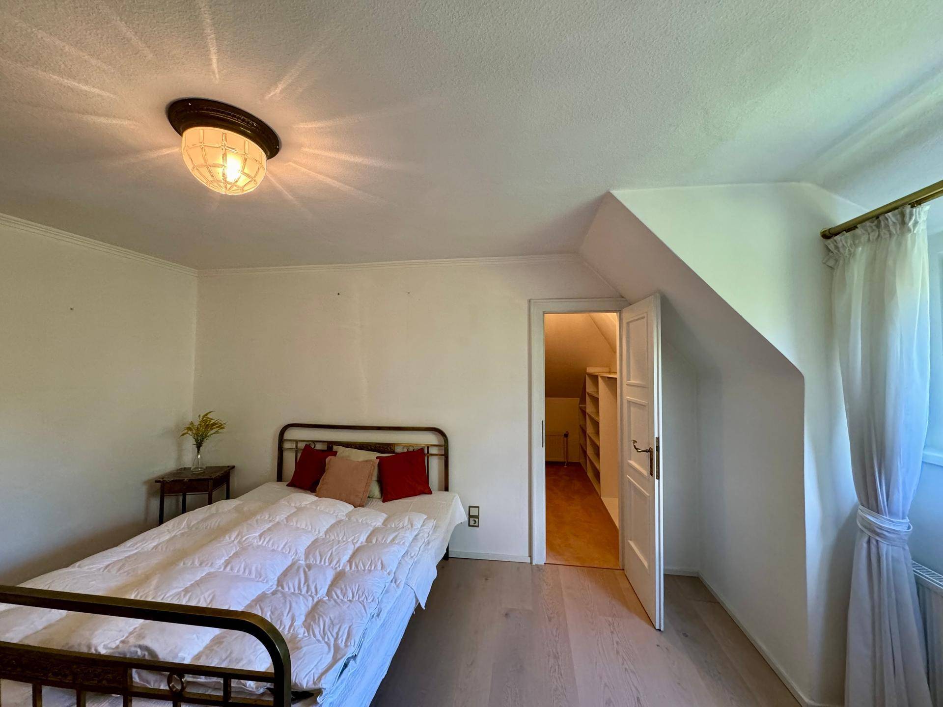 Helles Schlafzimmer mit Holzboden, Bett und Zugang zu einem begehbaren Kleiderschrank.