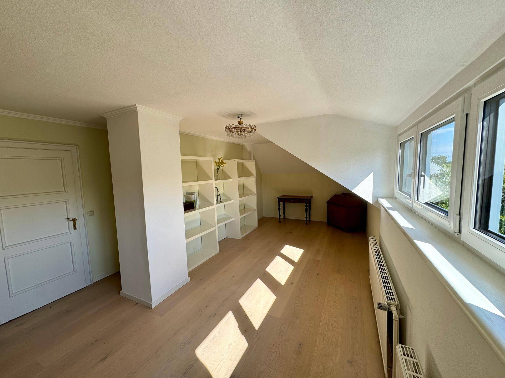 Helles Zimmer im Dachgeschoss mit Einbauregalen, Holzboden und Fenstern für viel Licht.