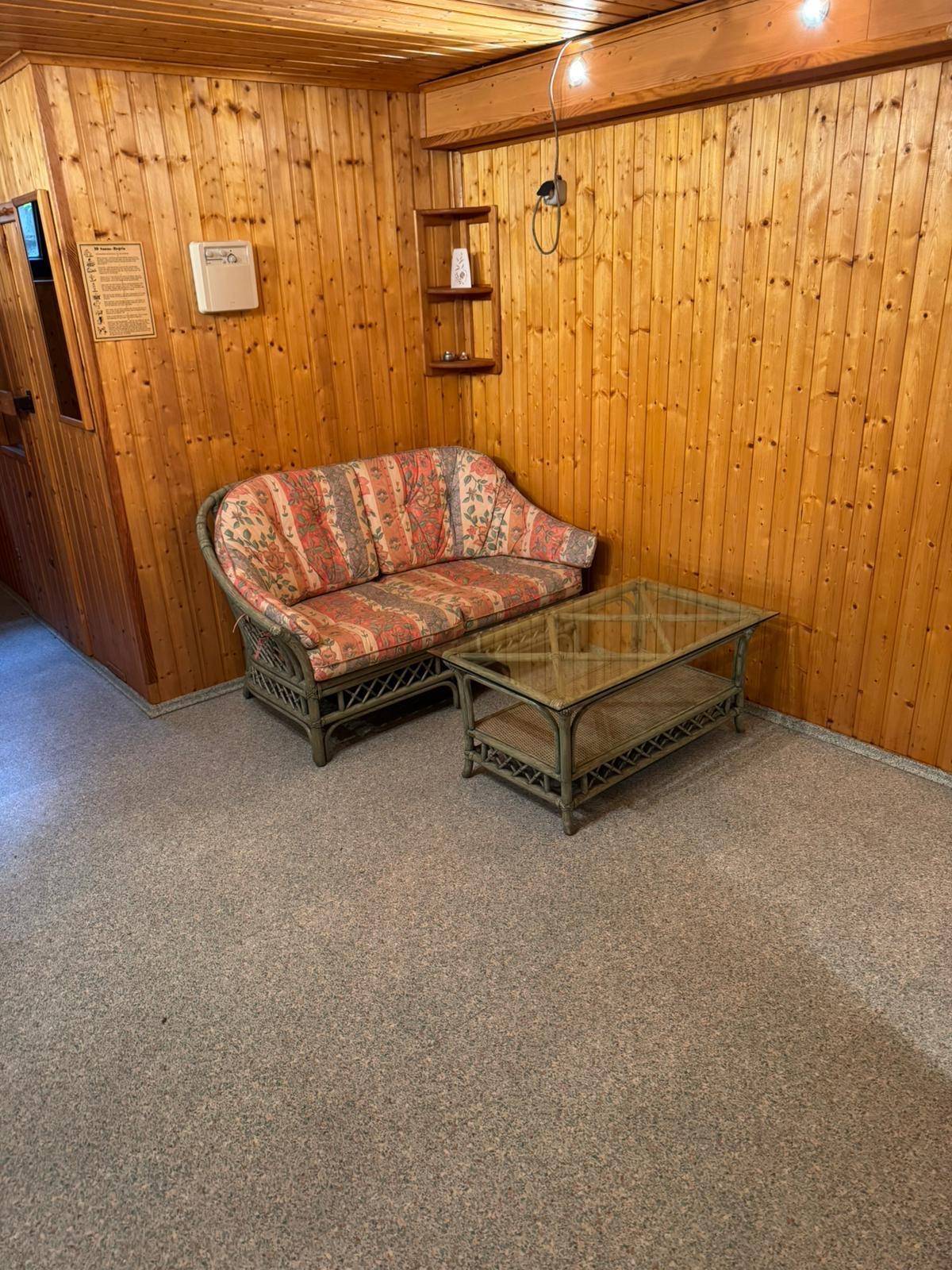 Gemütliches Rattansofa mit floralem Muster und Glastisch vor Holzvertäfelung.