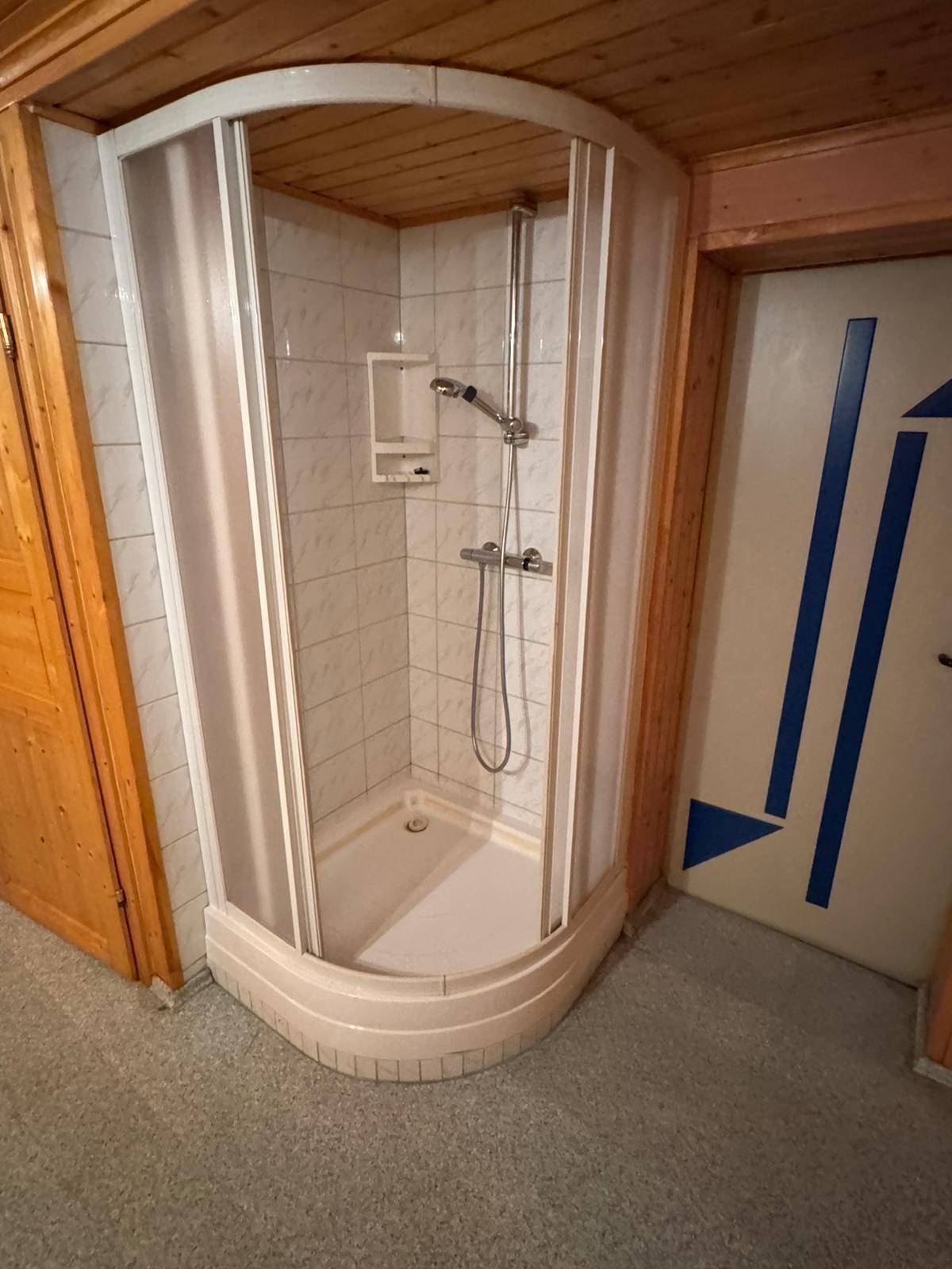 Eckduschkabine mit weißen Fliesen und Holzdecke in einem funktionalen Badezimmer.
